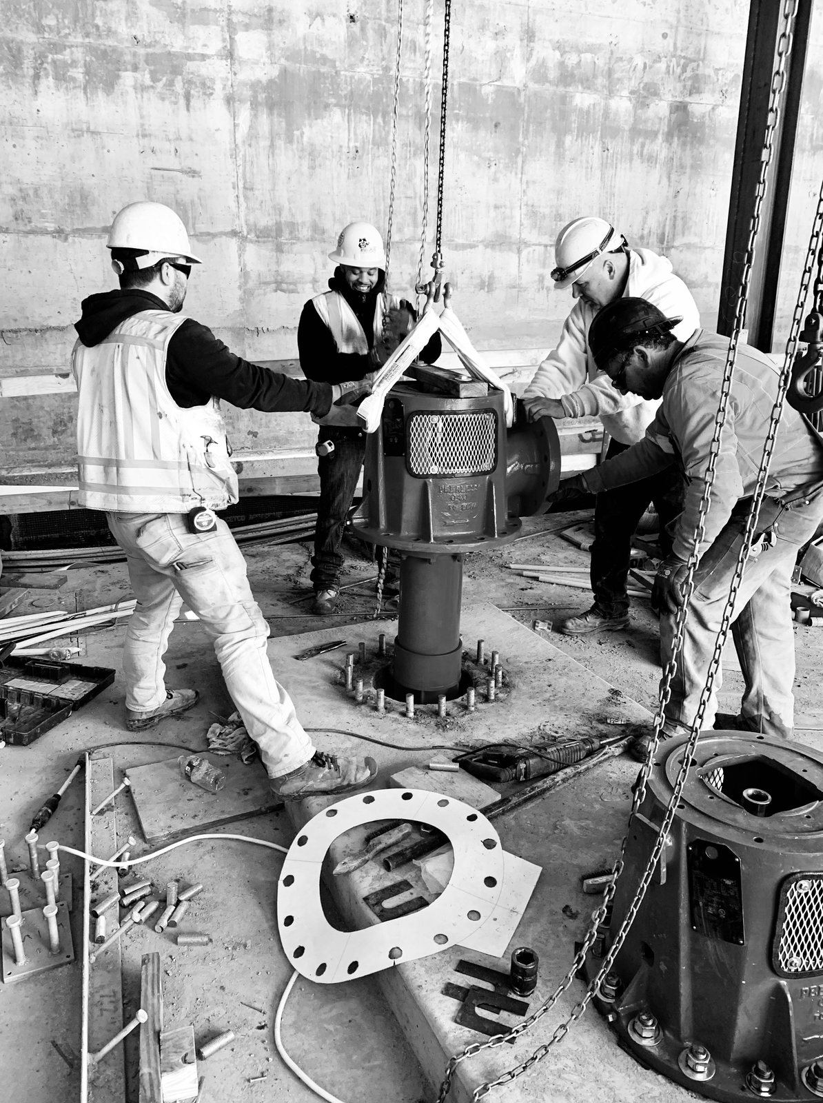 Crew setting a vertical fire pump head with a chain hoist, in black and white