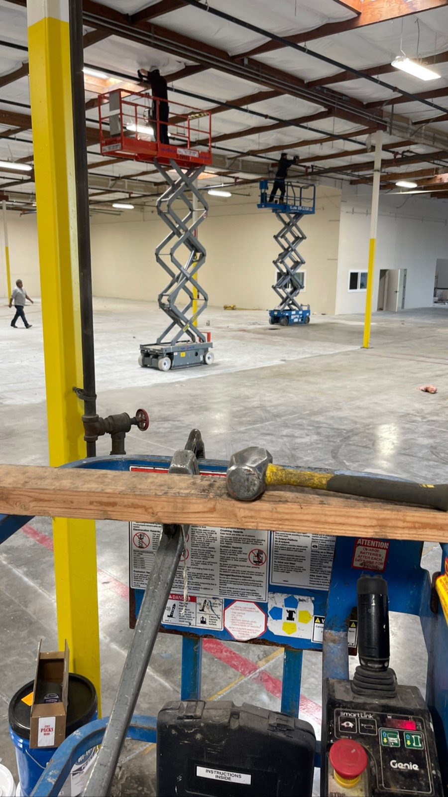 Crew working from scissor lifts at the ceiling of an open warehouse